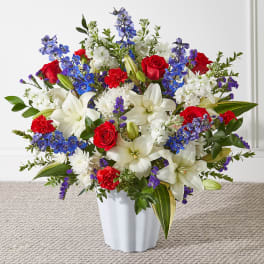 Mixed bouquet of red roses, white lilies, and blue flowers in a white vase