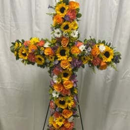 Cross-shaped floral tribute with sunflowers, orange roses, and mixed blooms