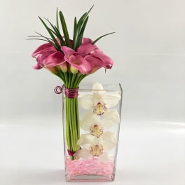 Pink calla lilies in a clear square vase with white orchids inside