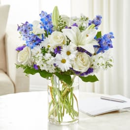White roses and lilies with blue flowers in a clear glass vase