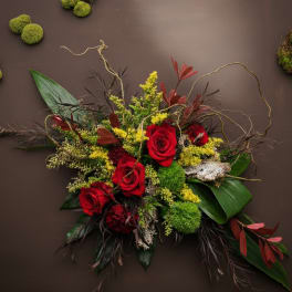 Asymmetrical arrangement of red roses with yellow accents, moss and bark on a dark brown background.