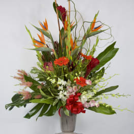 Tall tropical flower arrangement in a silver vase with orange and red blooms