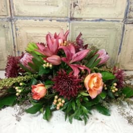 Low floral arrangement with pink lilies, peach roses, and burgundy blooms