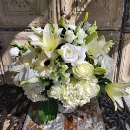 White floral arrangement with lilies, roses, hydrangeas, and a gerbera daisy in a vase