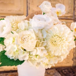White floral arrangement in a white vase with roses and orchids