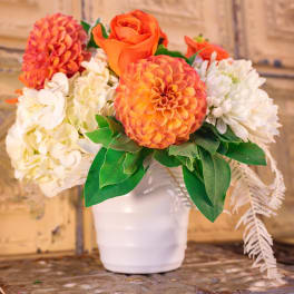 Orange and white floral arrangement in a white pot