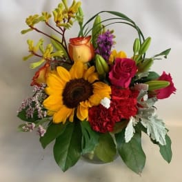 Mixed bouquet with a sunflower, roses, lilies, and carnations in a glass vase