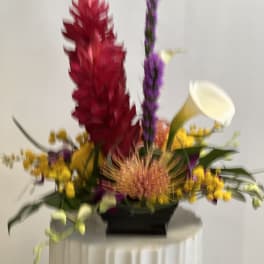 Colorful floral arrangement with red, purple, yellow, and white blooms in a black container