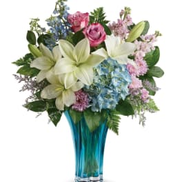 Bouquet of lilies, roses, hydrangea, and mixed blooms in a blue glass vase