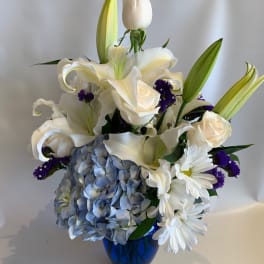 White lilies, roses, and blue hydrangea in a blue vase