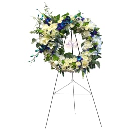 Standing wreath of white roses and mums with blue orchids on a metal easel
