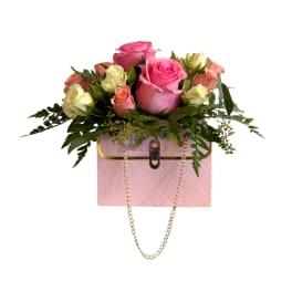 Pink and peach roses arranged in a pink box with a gold chain handle