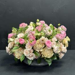 Low arrangement of pink and cream flowers in a dark bowl