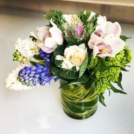 Mixed bouquet with orchids, roses, and blue flowers in a glass vase