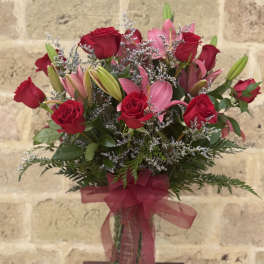 Bouquet of red roses and pink lilies in a glass vase with a ribbon