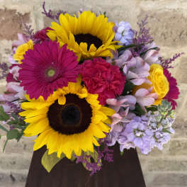 Bright mixed bouquet with sunflowers, gerbera daisies, and roses in a dark vase