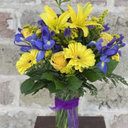 Yellow lilies, blue irises, and yellow daisies in a glass vase