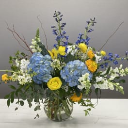 Blue hydrangeas with yellow and white flowers in a glass vase