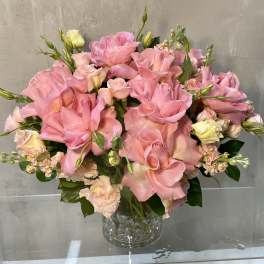 Pink roses and pale spray flowers arranged in a clear glass vase.