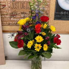 Mixed bouquet in a clear glass vase with yellow, red, and purple flowers