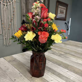 Mixed bouquet of red, yellow, and pink flowers in a dark glass vase