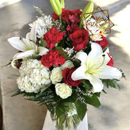 Red and white bouquet with lilies, roses, and a birthday topper in a glass vase