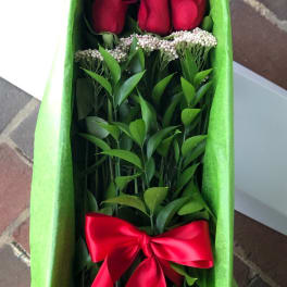 Boxed arrangement of long-stem red roses with a red satin bow in green tissue paper