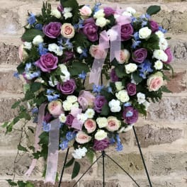 Heart-shaped floral wreath with purple, pink, and white roses on a stand