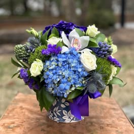 Blue hydrangeas, white roses, and purple flowers in a patterned vase