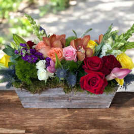 Mixed bouquet of roses, orchids, lilies, and snapdragons in a wooden planter