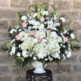 White floral arrangement with pink roses in a white urn vase