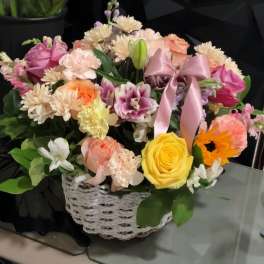 Mixed flower arrangement in a white wicker basket with a pink ribbon