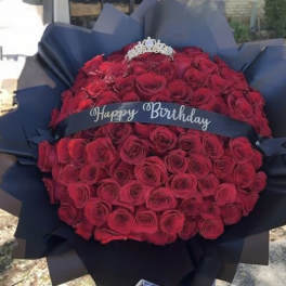 Bouquet of red roses wrapped in dark paper with a birthday ribbon