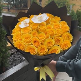 Bouquet of yellow roses with two white orchids wrapped in black paper