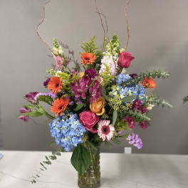 Mixed bouquet in a glass vase with bright orange, pink, blue, and purple flowers