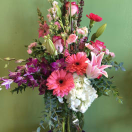 Tall mixed bouquet with pink lilies, gerbera daisies, orchids, and white hydrangea in a glass vase