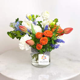 Mixed bouquet of orange and white flowers in a glass vase with a striped ribbon