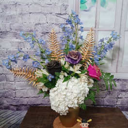 Arrangement of hydrangeas, roses, and blue flowers in a gold vase