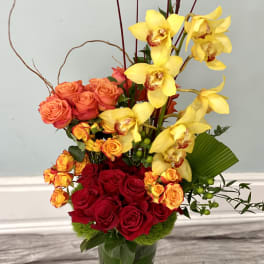 Red roses and yellow orchids in a tall glass vase