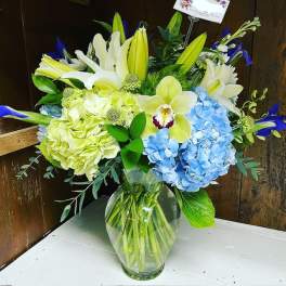 Bouquet of white lilies, blue hydrangeas, and orchids in a glass vase
