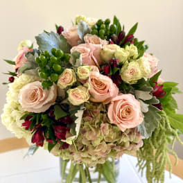 Round arrangement of blush roses, hydrangeas, and red flowers in a clear glass vase
