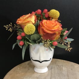 Orange roses in a white face vase with yellow pom flowers