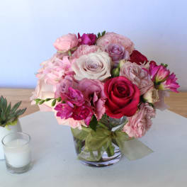 Pink and red rose bouquet in a glass vase beside a small succulent and candle