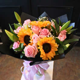 Bouquet of pink roses and sunflowers wrapped in black paper with a lavender ribbon