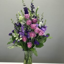 Pink roses and purple flowers arranged in a clear glass vase