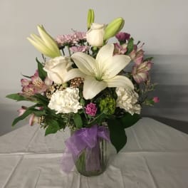 Bouquet of white lilies and pink flowers in a glass vase with a purple ribbon