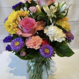 Mixed bouquet of pink, yellow, purple, and white flowers in a glass vase