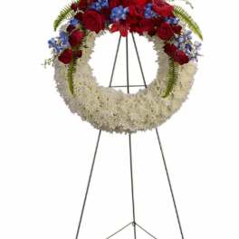 Standing floral wreath with red roses, white flowers, and blue accents on an easel