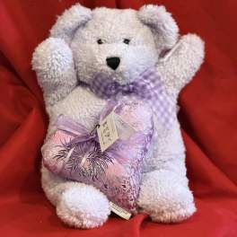 White teddy bear holding a lavender heart pillow on a red background