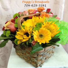 Basket of yellow sunflowers and mixed roses with green tissue wrap